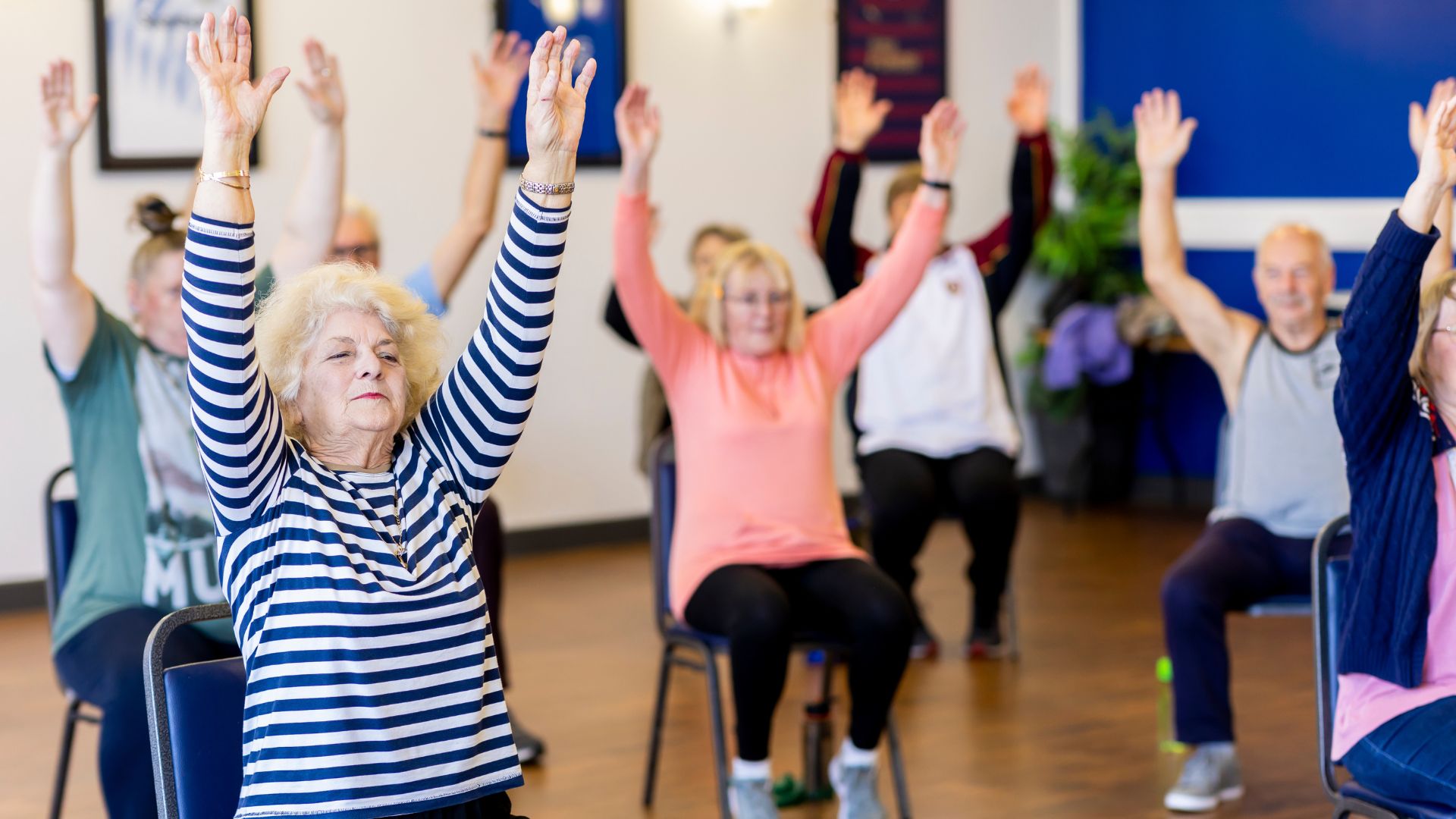 A group of people sitting in chairs with their arms raised in a fitness class.